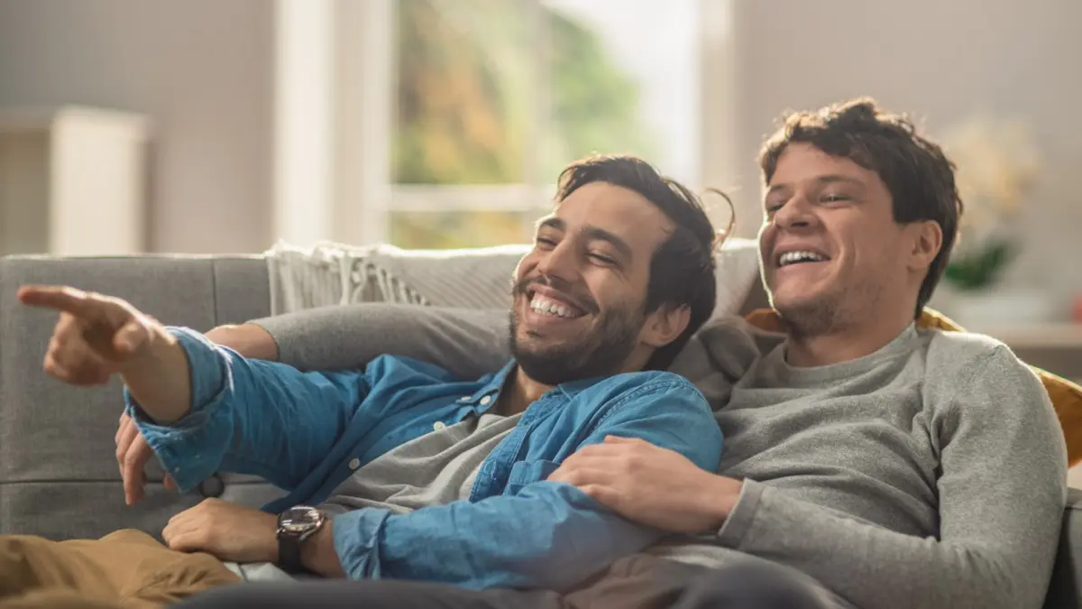 Two men laughing together on a couch at home